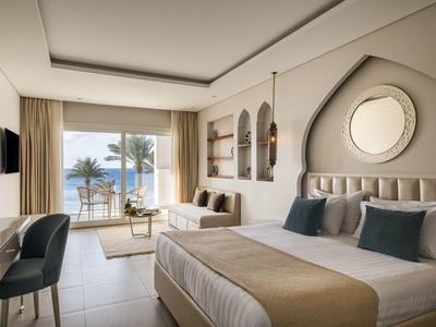 Chambre d'hôtel moderne avec lit double, coin salon et vue sur la mer à travers de grandes fenêtres.