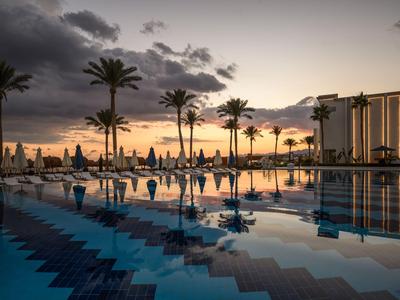 Area piscina dell'hotel con palme e ombrelloni al tramonto