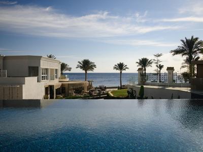 Hôtel avec piscine à débordement, palmiers et vue sur la mer sous un ciel clair.