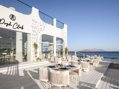 Restaurant en plein air avec vue sur la mer, mobilier blanc moderne et ciel dégagé.