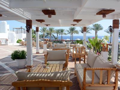Überdachte Terrasse mit bequemen Holzmöbeln und Blick auf Palmen und Meer im Hintergrund.