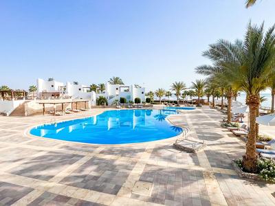 Moderner Hotelpool mit Liegestühlen und Palmen an sonnigem Strand.