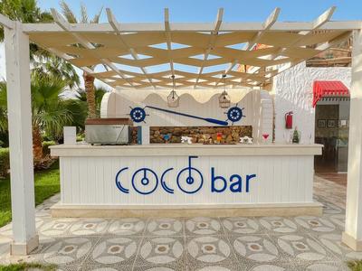 Moderner Coke Bar im Freien mit weißem Holz und Pergola bei Sonnenlicht.