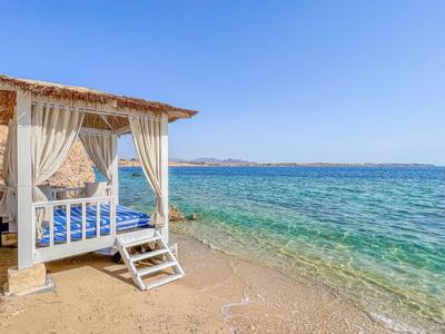 Strand mit weißem Pavillon mit Vorhängen und Blick auf klares Meer unter blauem Himmel.