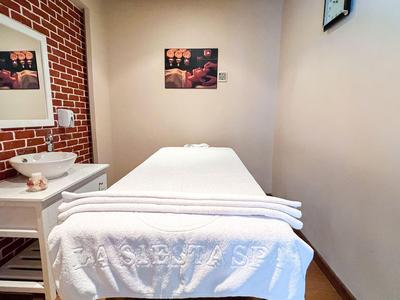 Weißes Massageliegenbett in einem schlichten, gemütlichen Raum mit Bildern an den Wänden.