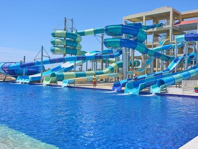Mehrere blaue Wasserrutschen führen in einen großen Pool vor einem Hotelgebäude.