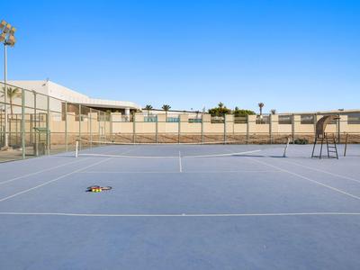 Blick auf einen leeren Tennisplatz mit Zaun und Beleuchtung bei klarem Himmel.