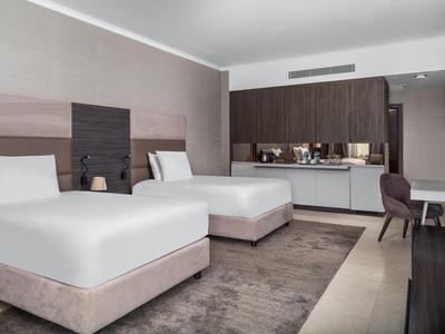 Modernes Hotelzimmer mit zwei Einzelbetten, Schreibtisch und Minibar in neutralen Farben.