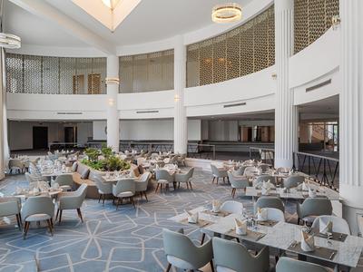 Helles, modernes Hotelrestaurant mit rundem Sitzbereich und großen Fenstern.