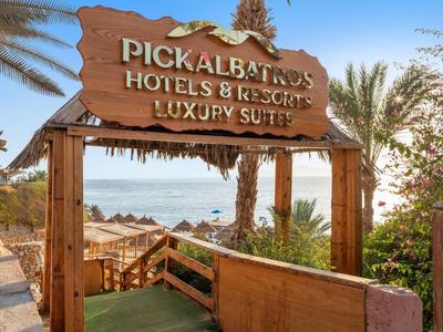 Holzschild mit Hotelname über einem Pfad, der zu Strandliegen am Meer führt.