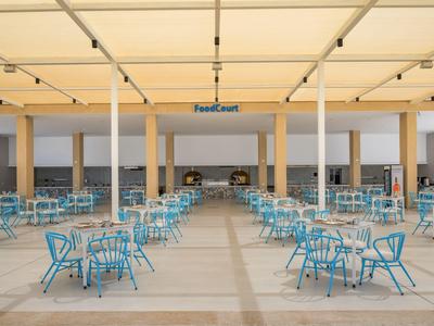 Freiluft-Essbereich eines Hotels mit blauen Stühlen und Beistelltischen unter einem großen weißen Sonnendach.