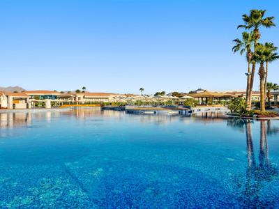 Großer blauer Pool mit Palmen und Hotelgebäuden unter klarem Himmel.