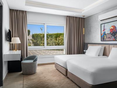 Helles Hotelzimmer mit zwei Einzelbetten, Fenster mit Blick auf grüne Bäume und moderne Einrichtung.
