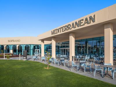 Außenbereich eines Hotels mit moderner Lounge und mediterranem Schriftzug an sonnigem Himmel.