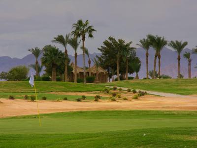 Grüner Golfplatz mit Palmen und bewölktem Himmel im Hintergrund eines Hotelareals.
