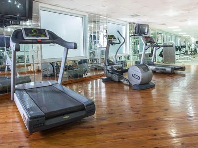 Innenraum eines Fitnessraums mit Laufband, Crosstrainer und Spiegelwand auf Holzfußboden.