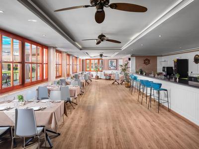 Moderner Speisesaal mit großen Fenstern, Holzboden und Deckenventilatoren in einem Hotel.