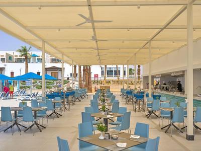 Offenes, überdachtes Restaurant mit blauen Stühlen und Tischen in einem Hotelkomplex.