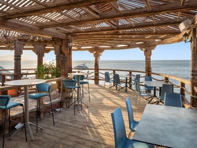 Offener Holzpavillon mit Tischen und blauen Stühlen mit Meerblick.