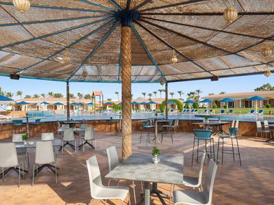 Überdachte Außenbar mit Tischen und Stühlen neben einem Pool in einem Hotelresort.