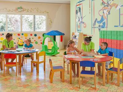Kinder spielen und malen an Tischen in einem hellen, farbenfrohen Kinderzimmer im Hotel.