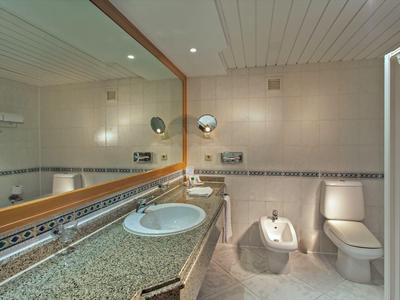 Helles Badezimmer mit Waschbecken, Bidet, Toilette und großem Spiegel über der Arbeitsplatte.