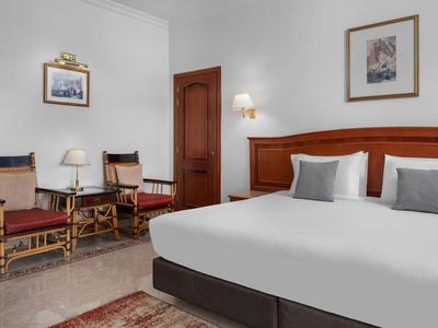 Helles Hotelzimmer mit großem Bett, zwei Stühlen und Wanddekorationen.