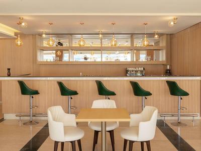 Area bar dell'hotel moderna con pannelli in legno chiaro, sgabelli verdi e sedie bianche.