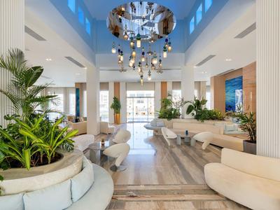 Sala lounge dell'hotel luminosa con sedie moderne, piante verdi e lampada da soffitto scenografica.