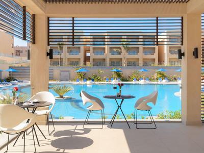 Terrazza con tavoli rotondi e sedie accanto a una piscina all'aperto e edifici dell'hotel sullo sfondo.