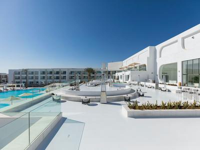 Modernes Hotel mit großem Pool, weißer Terrasse und klar blauem Himmel.