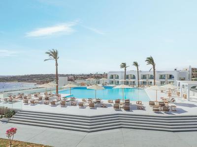 Moderner Hotelpool mit Liegestühlen, Palmen und Meerblick unter blauem Himmel.