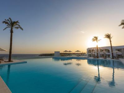 Atmospärischer Poolbereich mit Palmen und Sonnenuntergang an einem Resort am Meer.