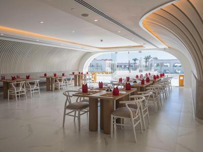 Modernes Hotelrestaurant mit geschwungenen Decken und hellen Holzmöbeln, dekoriert mit roten Servietten.