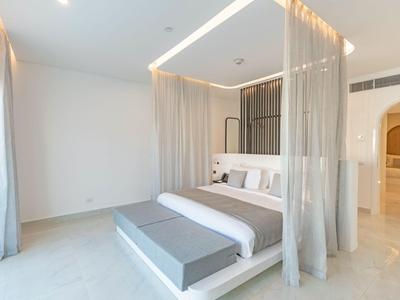 Helles Schlafzimmer mit vierpfostenbett, grauer Bank und transparenten Vorhängen in modernem Hotel.