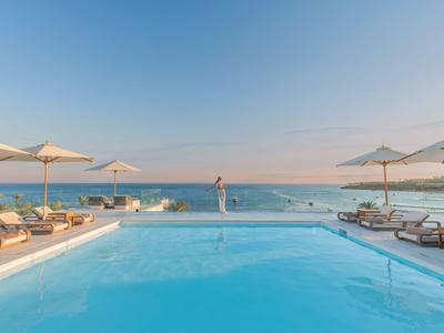 Moderner Pool mit Sonnenliegen und Schirmen mit Blick auf das ruhige Meer unter klarem Himmel.