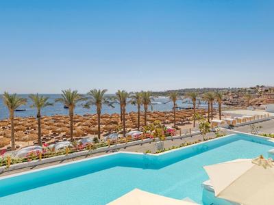 Hotelpool mit Blick auf den Strand, Palmen und die blaue Küste.