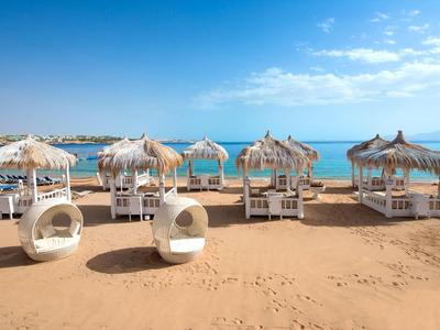 Strand mit weißen Sonnenliegen und strohgedeckten Sonnenschirmen am klaren blauen Meer.