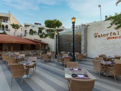 Hoteleigene Terrasse mit Stühlen und Tischen vor einer künstlichen Wasserfallwand.