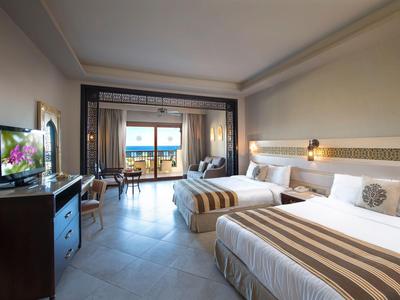 Modernes Hotelzimmer mit zwei Betten, Fernseher, Stühlen und Balkon mit Meerblick.