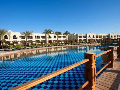 Ein weitläufiges Hotel mit einem großen blauen Schwimmbecken und einer Holzbrücke im Vordergrund.