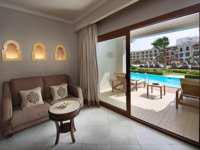 Gemütlicher Sitzbereich neben bodentiefen Fenstern mit Blick auf einen Hotelpool und Außenbereich.