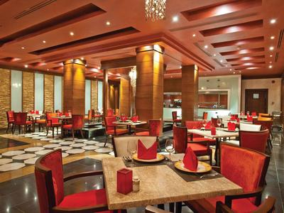 Elegantes Hotelrestaurant mit roten Stühlen, Holztischen und warmem Deckenlicht.