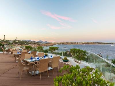 Terrasse mit Stühlen und Tischen mit Blick auf das Meer bei Sonnenuntergang.