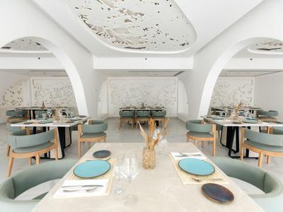 Ristorante moderno e luminoso con tavoli rotondi, sedie verdi e pareti bianche decorative.