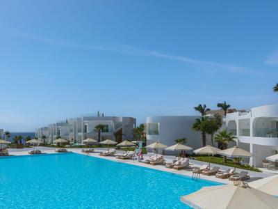 Grande piscina blu con edifici dell'hotel bianchi e ombrelloni sotto un cielo limpido.