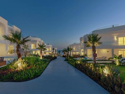 Vista serale di un resort moderno illuminato con palme e un sentiero su entrambi i lati.
