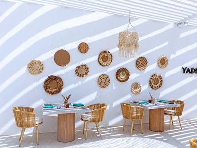 Terrazza moderna con pareti bianche, tavoli in legno, sedie intrecciate e decorazioni da parete.