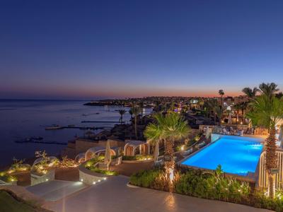 Terrazza dell'hotel con piscina illuminata e vista sul mare al tramonto.