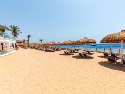 Ampia spiaggia sabbiosa con lettini, ombrelloni di paglia e cielo azzurro limpido vicino al mare.